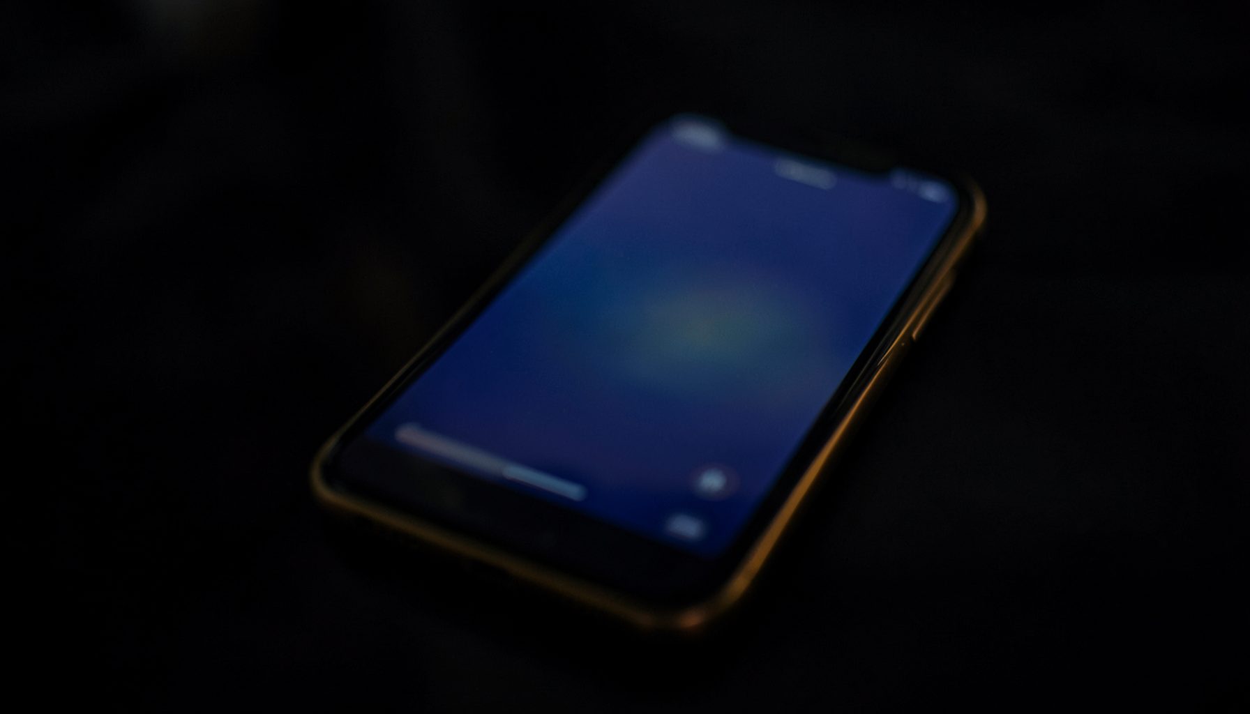 A smartphone glowing softly in navy and gold tones against a dark blurred background, evoking a calm nighttime app-download mood