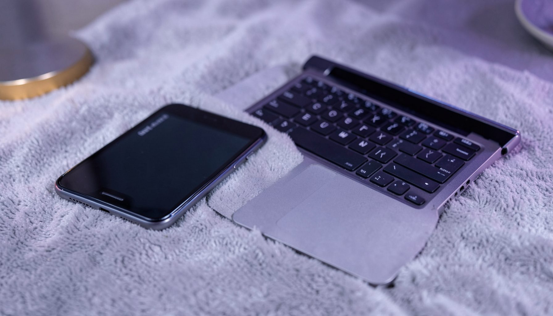 Smartphone and laptop resting on a soft grey surface with lavender and gold accent lighting, calm technology mood