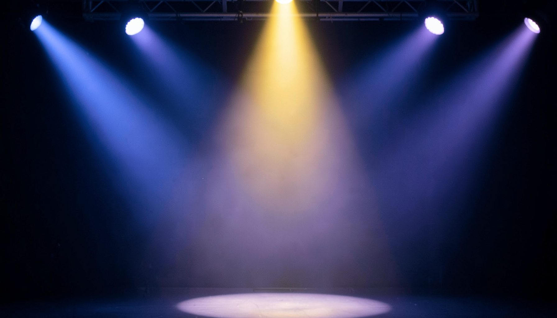 Soft navy and lavender toned stage lighting with a warm gold spotlight, evoking a glamorous entertainment atmosphere